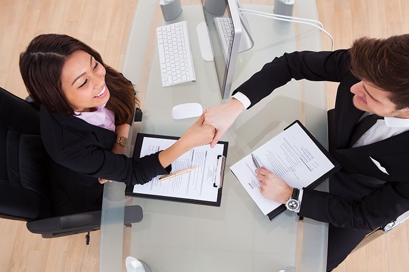shaking-hands-job-hire woman shaking hands with male sitting at desk